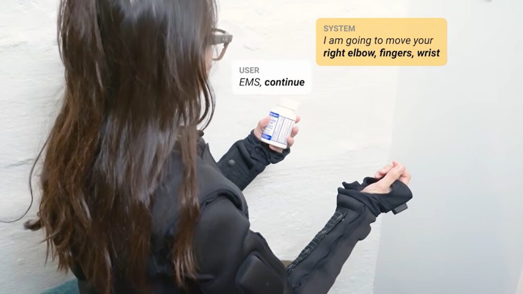 A woman gave the command 'open this.' The system evaluated and responded, then the command 'continue' was given, after which the suit opens the jar. Photo.