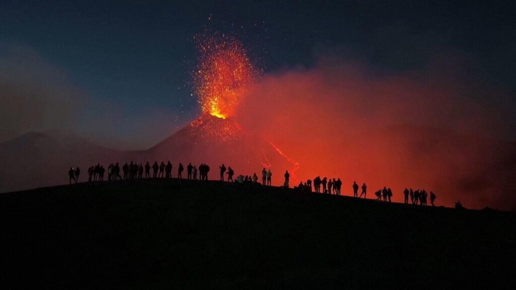 People against the backdrop of Mount Etna erupting, coast of Sicily. Photo.