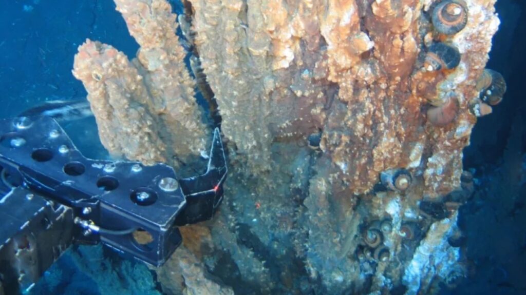 A robotic arm breaks off a piece of mineral-rich rock deep underwater. Photo.