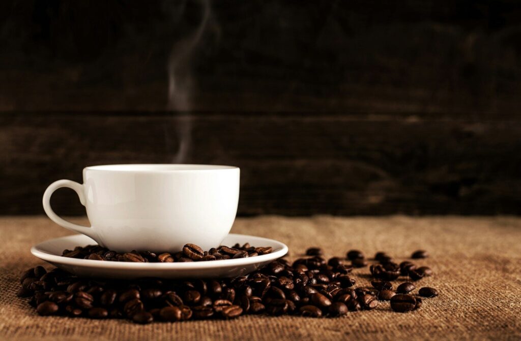 A cup of hot coffee surrounded by coffee beans on a table