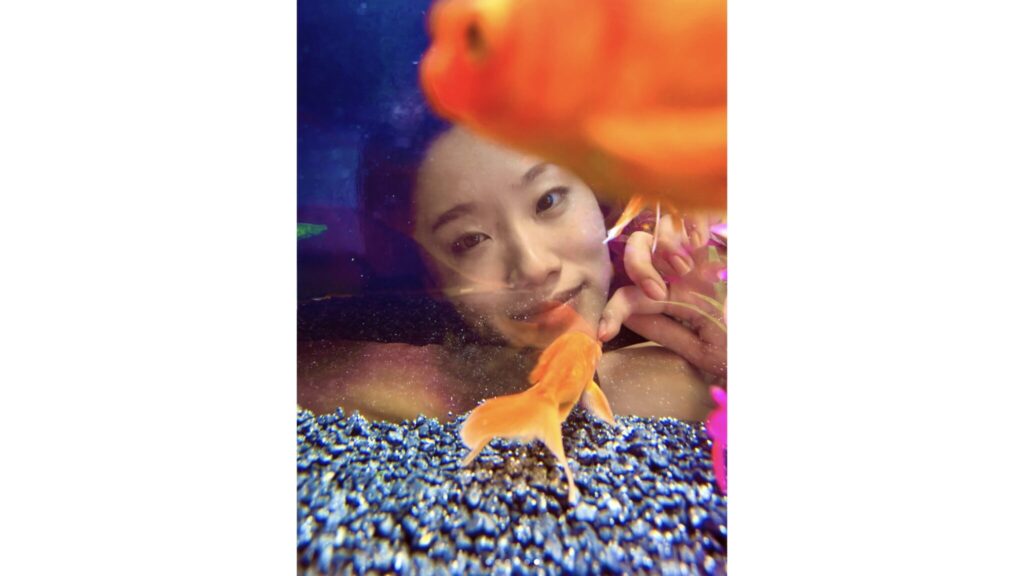 A woman looking at a goldfish through aquarium glass