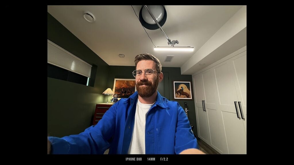 A man photographing himself with the iPhone Duo's rear ultra-wide camera in a room with green walls