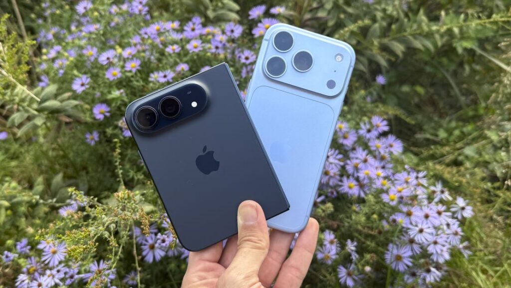 A dark blue iPhone Duo and a light blue iPhone 18 Pro held in hand against blooming asters